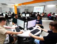 Alunos de Ciência da Computação em aula prática colaborativa no laboratório de criação, trabalhando em grupo em computadores para desenvolver projetos de software e tecnologia.