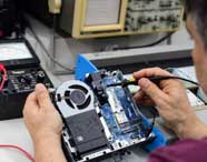 Especialista em Ciência da Computação realizando manutenção e teste de hardware em um mini computador, utilizando equipamentos de medição em laboratório de arquitetura de sistemas.