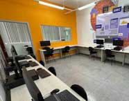 "Laboratório de Ciência da Computação equipado para o ensino de programação e desenvolvimento, com estações de trabalho e um mural ilustrando conceitos de TI como HTTPS, SQL e IA.  "