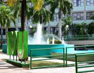Espaço externo do campus da Unoeste em Presidente Prudente, com fonte de água central, palmeiras altas, gramado verde e letreiro verde “I ♥ U”. O cenário transmite sensação de acolhimento, modernidade e integração com a natureza.
