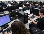 Alunos da faculdade de Análise e Desenvolvimento de Sistemas em aula prática de programação Python no laboratório, desenvolvendo códigos e sistemas.