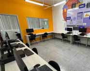 Laboratório equipado para o curso de Análise e Desenvolvimento de Sistemas, com estações de trabalho e mural ilustrando conceitos de programação como SQL, IA e cibersegurança.