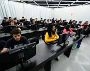Faculdade de Análise e Desenvolvimento de Sistemas: sala de aula moderna no campus de Presidente Prudente, com alunos concentrados em computadores. O ambiente iluminado, mobiliário preto e teto com iluminação geométrica valorizam a infraestrutura tecnológica do curso, reforçando a prática e o ensino atualizado em tecnologia.