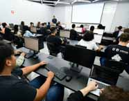Faculdade de Análise e Desenvolvimento de Sistemas: alunos durante aula prática em laboratório de informática no campus Presidente Prudente. Ambiente moderno, com computadores e professor interagindo, destacando o ensino tecnológico e a preparação para o mercado de TI.