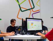 Faculdade de Análise e Desenvolvimento de Sistemas em Presidente Prudente, alunos reunidos em laboratório de informática com computadores, participando de atividade prática de programação e desenvolvimento. O ambiente moderno e colaborativo destaca a integração entre teoria e prática no curso.