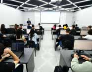 Faculdade de Análise e Desenvolvimento de Sistemas em Presidente Prudente, sala de aula com estudantes utilizando computadores durante atividade guiada por professor, reforçando o foco do curso em prática, inovação e aprendizado em ambientes tecnológicos.