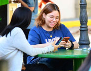 Alunos da Faculdade de História em Presidente Prudente interagindo em área de convivência externa, sentados em mesas redondas verdes.