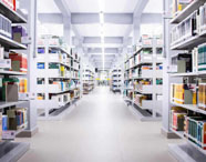 Corredor da biblioteca da Faculdade de História em Presidente Prudente, com prateleiras repletas de livros, em ambiente amplo e iluminado.