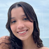 Imagem de Gabriela, aluna do curso de enfermagem no campus Guarujá. O fundo apresenta tons azulados suaves, criando um contraste agradável e moderno que remete a um ambiente acadêmico ou institucional. A iluminação clara contribui para destacar o cenário, reforçando o compromisso de Gabriela com sua formação na enfermagem.