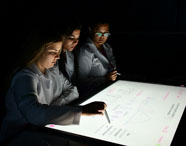 Grupo de alunos da Enfermagem utilizando mesa interativa na sala Betha, em atividade prática. 