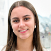 Imagem de Julia, aluna do curso de fisioterapia no campus Guarujá, vestindo jaleco branco. O fundo é claro e iluminado, com detalhes de equipamentos médicos ao fundo, sugerindo um ambiente acadêmico voltado para práticas fisioterapêuticas.