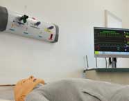 Manequim adulto deitado em maca de simulação hospitalar, com painel de gases na parede e monitor cardíaco ligado ao lado. A cena representa ambiente de aula prática do curso de Fisioterapia, focada em atendimento respiratório e monitorização.