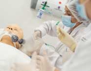 Detalhe de estudantes de Fisioterapia durante simulação de emergência respiratória, utilizando manequim adulto, ambu e tubo orotraqueal. O ambiente é limpo, bem iluminado e equipado, próprio para aulas práticas da graduação.