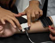 Close-up das mãos de um profissional ou estudante de Fisioterapia aplicando eletrodos de estimulação em um pulso para tratamento fisioterapêutico.