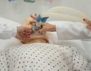 Mãos de duas alunas de Fisioterapia em jalecos brancos posicionando uma máscara de oxigênio em um manequim de paciente para simulação de ventilação.