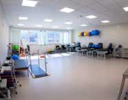 Visão panorâmica de um amplo laboratório ou clínica de Fisioterapia equipado com macas, bolas terapêuticas, barras paralelas, halteres e rampas para reabilitação.