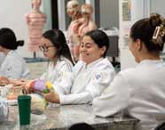 Alunas do curso de Psicologia em jalecos brancos interagindo com modelos anatômicos coloridos de cérebro em aula prática, com entusiasmo e foco.