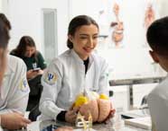 Aluna de Psicologia em jaleco branco sorrindo e apresentando um modelo anatômico detalhado do cérebro para colegas em aula prática.