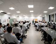 Ampla sala de aula ou laboratório de Psicologia com vários alunos em jalecos brancos assistindo a uma aula prática sobre anatomia cerebral, com professor demonstrando e recursos visuais.