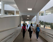 Três estudantes caminham por uma rampa interna acessível da Unoeste Jaú, cercada por corrimãos metálicos e paredes brancas. O ambiente é amplo, moderno e iluminado, com plantas decorativas ao fundo e grandes janelas de vidro, transmitindo sensação de integração e movimento universitário.