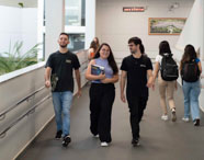 Alunos circulam pela rampa interna da Unoeste Jaú, ladeada por corrimãos metálicos e vegetação decorativa. O ambiente é aberto, com luz natural, paredes brancas e sensação de acessibilidade, favorecendo o fluxo de estudantes entre as áreas do campus