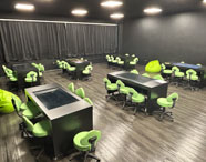 Sala Betha da Unoeste Jaú, equipada com mesas digitais pretas, cadeiras giratórias verdes e pufes. O ambiente é tecnológico, com cortinas pretas, piso escuro e disposição voltada para atividades práticas e colaborativas, ideal para aulas inovadoras do curso de Nutrição.