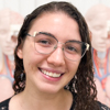 Imagem de Katley, aluna do curso de fisioterapia no campus Jaú, trajando blusa escura. O fundo figuras de anatomia, indicando um ambiente interno iluminado e organizado, propício para estudos e práticas acadêmicas.