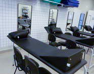 Sala de clínica de Fisioterapia equipada com várias macas de tratamento pretas, espelhos quadriculados e material para exercícios de reabilitação.