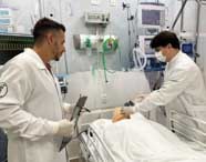 Professor e estudante do curso de Fisioterapia da Unoeste, ambos de jaleco branco, simulam atendimento hospitalar em manequim adulto deitado em leito. O ambiente reproduz UTI, com monitores, bombas de infusão e equipamentos médicos modernos, proporcionando realismo à prática