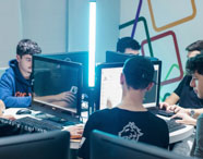 Alunoz da Faculdade de Ciência de Dados observam atentamente monitor de computador, onde há código aberto e janelas de software. Ele está sentado em laboratório moderno, com outros estudantes ao fundo, evidenciando o ensino prático e digital da área de dados em Presidente Prudente.