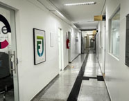 Corredor interno da FIPP, Faculdade de Informática de Presidente Prudente, com paredes brancas, piso claro e placas de identificação nas portas. À esquerda, sala envidraçada com logotipo “code” e cadeira de escritório, transmitindo ambiente limpo, moderno e funcional.