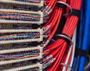 Detalhe de infraestrutura de rede da Faculdade de Ciência de Dados, mostrando cabos organizados em cores vermelha, azul, branca e laranja conectados a painéis de distribuição. A imagem evidencia a estrutura tecnológica avançada utilizada nos laboratórios da Unoeste.