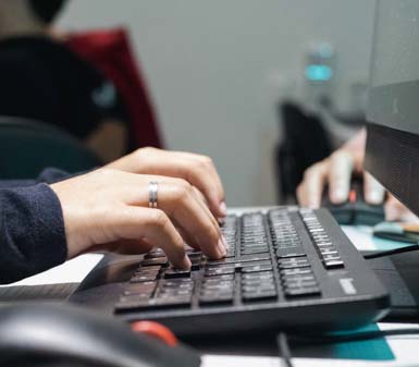 Mãos de estudante digitando em teclado preto diante de monitor de computador, com foco no ambiente tecnológico. O cenário sugere uma aula prática do curso de Ciência de Dados em Presidente Prudente, Unoeste, evidenciando o uso de tecnologia e análise de dados em laboratório moderno.