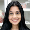 Isabela, aluna do curso de biomedicina no campus Guarujá. O cenário ao fundo inclui armários e prateleiras com materiais de estudo, reforçando o ambiente acadêmico e técnico. A composição transmite foco e dedicação à formação biomédica.