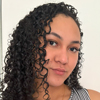 Karolline, aluna do curso de biomedicina no campus Guarujá, trajando camiseta cinza. Ela está em um ambiente interno com fundo totalmente claro e bem iluminado, transmitindo uma atmosfera limpa e profissional, típica de espaços acadêmicos voltados para a área da saúde.