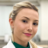 Suzana, aluna do curso de biomedicina no campus Jaú, trajando jaleco branco. Ela está em uma sala de aula com fundo claro e paredes brancas, transmitindo um ambiente acadêmico organizado e voltado para o aprendizado na área da saúde.