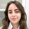 Thais, aluna do curso de biomedicina no campus Jaú, trajando jaleco branco. O fundo apresenta prateleiras com materiais acadêmicos e um ambiente iluminado, sugerindo um laboratório ou sala de estudos técnicos. A composição reflete o comprometimento com a formação biomédica.