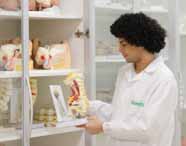 Curso de Biomedicina: Aluna de cabelos escuros presos, com óculos e jaleco branco, sorri enquanto observa um modelo anatômico de torso humano em um laboratório moderno, com prateleiras ao fundo, compondo um cenário de aula prática, limpo e organizado.
