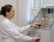 Faculdade de Biomedicina: Aluna de cabelos presos, com óculos e jaleco branco, opera um equipamento de análise laboratorial com frascos de vidro, em um laboratório moderno, compondo um cenário de aula prática, limpo e organizado.