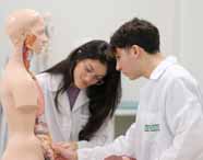 Faculdade de Biomedicina: Alunos com jalecos brancos Unoeste, observam e interagem com um modelo anatômico de torso humano em um laboratório moderno, com esqueletos ao fundo, compondo um cenário de aula prática, limpo e organizado. 