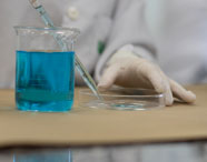 Detalhe de atividade laboratorial com líquido azul em béquer durante aula prática em Jaú. 