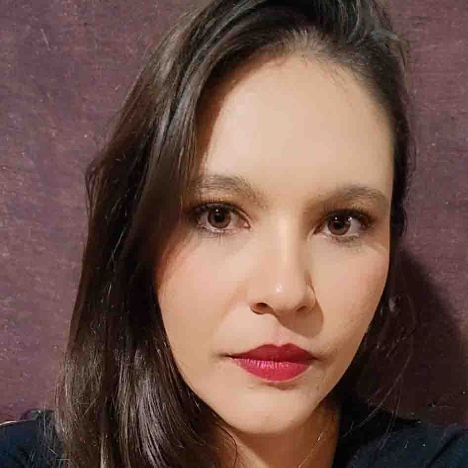 Dahiara, egressa de Ciências Biológicas - Licenciatura, posando em um ambiente interno com um fundo escuro. Ela tem cabelos castanhos escuros e usa batom vermelho, com uma expressão séria.