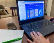 Faculdade de administração em Guarujá biblioteca online: pessoa acessa uma biblioteca virtual pelo notebook, com caderno e caneta Unoeste ao lado, sobre mesa de madeira. O ambiente doméstico é confortável, mostrando integração entre tecnologia, materiais de estudo e autonomia do estudante, facilitando a busca por conhecimento acadêmico em qualquer lugar.
