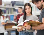 Faculdade de administração em Jaú, biblioteca: alunos exploram prateleiras repletas de livros, lendo e pesquisando juntos em ambiente amplo, moderno e bem iluminado. A cena evidencia o acesso a materiais didáticos de qualidade, a colaboração entre colegas e o incentivo à pesquisa e ao aprofundamento acadêmico no curso de administração.