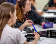 Alunos da Faculdade de Letras Português acompanhando aula em sala, com foco em estudante segurando caneta azul, representando o aprendizado e a interação.