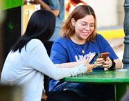 Alunos da Faculdade de Letras Português em Presidente Prudente interagindo em área de convivência externa, sentados em mesas redondas verdes.