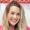 Imagem de Blanda, egressa do curso de Psicologia da Unoeste, vestindo uma blusa rosa. O fundo apresenta tons de branco e alaranjados com um quadro branco, sugerindo um ambiente institucional ou acadêmico. A composição reflete profissionalismo e conexão com a área de formação.