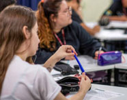 Alunos da Faculdade de Letras Inglês acompanhando aula em sala, com foco em estudante segurando caneta azul, representando o aprendizado e a interação.