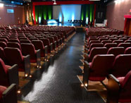 Interior do Teatro César Cava, palco de eventos acadêmicos da Faculdade de Letras Inglês, com poltronas vazias e palco iluminado.