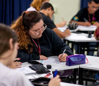 Aluna da Faculdade de Letras Inglês em Presidente Prudente concentrada em anotações durante aula, ilustrando o perfil profissional do curso focado em estudo, escrita e comunicação.